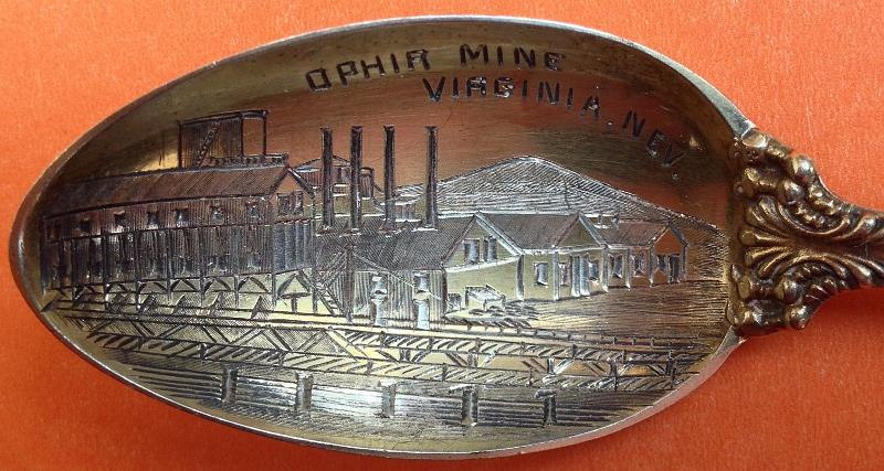 Souvenir Mining Spoon Bowl Ophir Mine Virginia City Nev.JPG - SOUVENIR MINING SPOON OPHIR MINE VIRGINIA CITY NEVADA- Sterling silver souvenir spoon, commemorating the Ophir Mine, Virginia City, Nevada, handle in a very nice pattern, gold finished bowl with hand engraved scene of mining building complex with smoke stacks and railroad tracks in the front, marked OPHIR MINE, VIRGINIA NEV., measures 5 5/8 in. long, back marked STERLING PAT. 1898 and maker’s mark of Towle Manufacturing Co. [The Comstock Lode is a lode of silver ore located under the eastern slope of Mt. Davidson, a peak in the Virginia Range in Nevada. It was the first major discovery of silver ore in the United States.  After its discovery in 1859, mining camps soon thrived in the vicinity, which became bustling centers of fabulous wealth, including Virginia City and Gold Hill. In 1857, the Grosh brothers, Ethan and Hosea, discovered a vein of ore on the slope of Mt. Davidson, but died before they could develop their mine.  They left a trunk with ore samples and documentation with another local prospector, Henry Comstock.  In 1859, Peter O’Riley and Pat McLaughlin discovered silver while prospecting for gold in the same area.  Assays confirmed the richness of the find.  Comstock, remembering the contents of the abandoned trunk, used an accusation claim jumping to gain a partnership with O’Riley and McLaughlin and three others.  Their discovery would become the fabulous Ophir Mine, the first of several mines developed along a north-to-south corridor from above Virginia City to below Gold Hill that would define the Comstock Lode. Like many prospectors in those days, the original partners sold their shares early and did not benefit from the riches yet to be mined.  As was common with the Comstock mines, the rock in the Ophir Mine was soft and easily collapsed into the working stopes. Unlike most silver ore deposits, which occur in long thin veins, those of the Comstock Lode occurred in discrete masses often hundreds of feet thick. The ore was so soft it could be removed by shovel. Although this allowed the ore to be easily excavated, the weakness of the surrounding material resulted in frequent and deadly cave-ins. The excavations were carried to depths of more than 3,200 feet.  The cave-in problem was solved in 1860 by the method of square set timbering invented by Philip Deidesheimer, a German mining engineer, who had been appointed superintendent of the Ophir Mine.  Using Deidesheimer’s invention, as ore was removed it was replaced by timbers set as a cube six feet on a side. Thus, the ore body would be progressively replaced with a timber lattice. Often these voids would be re-filled with waste rock from other diggings after ore removal was complete. By this method of building up squares of framed timbers, an ore vein of any width could be safely worked to any height or depth. Deidesheimer refused to patent his invention and eventually was bankrupted by speculation in mining stocks in 1878.  Production in the Comstock Lode mines peaked in 1877 but mining continued into the later-1900’s.  About 192 million ounces of silver and about 8.3 million ounces of gold were produced from the Comstock Lode from 1859-1986.  Eighty percent of this production was prior to 1880.  At the time of production the precious metal value totaled $412 million.  At 2009 prices, the total value was about $11 billion with $3 billion in silver and $8 billion in gold.  Huge individual fortunes were made through the Comstock Lode.  Four Irishmen, John W. Mackay, James G. Fair, James C. Flood and William S. O’Brien, formed a business partnership, the Consolidated Virginia Mining Company, in Virginia City which dealt in silver stocks and operation of mines on the Comstock Lode. These four men became known as the Silver Kings of the Comstock.  In addition, George Hearst, a future US Senator from California, became a partner in the largest private mining firm in the US which owned and operated the Ophir Mine as well as other gold and silver mining interests that established his fortune.  William C. Ralston, founder of the Bank of California, and his partner William Sharon, Nevada agent for the Bank of California, both made enormous profits from the Comstock Lode.  William M. Stewart, who abandoned mining to become a wealthy attorney in Virginia City, Nevada, participated in mining litigation and the development of mining on the Comstock Lode. As Nevada became a state in 1864, Stewart assisted in developing its constitution, and became the first United States Senator from Nevada.]
